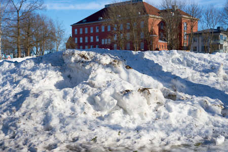 A collected dirty snow with an old brick house in the background.