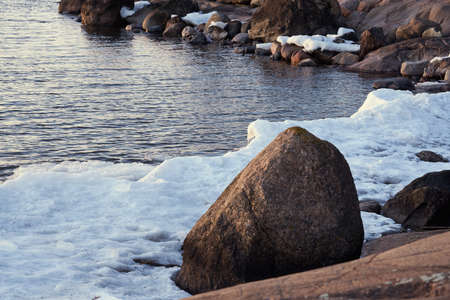 The stone coast of the Baltic Sea in spring with the remains of ice in sunlight.