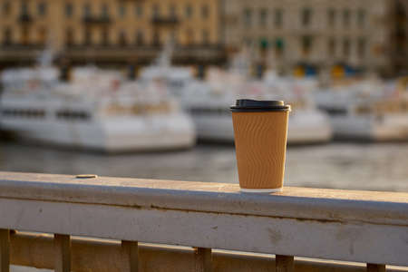 A paper cup of coffee with a harbor on a blurred background.の写真素材