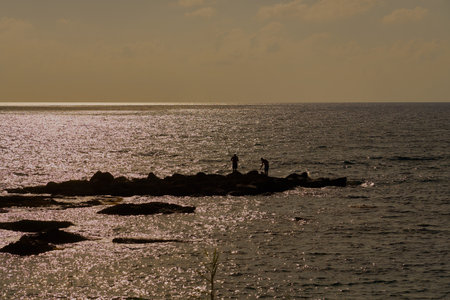 Silhouettes of fishermen on the stone shore of the Mediterranean Sea at sunsetの写真素材