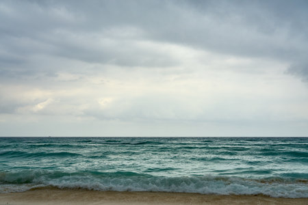 Waves and foam on a tropical sandy beach with clouds.の写真素材