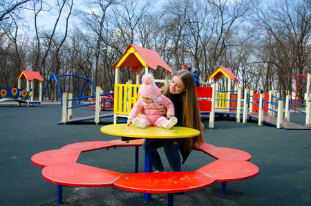 Mom plays on a bright playground with a small child in the street, nomads, a house during the day