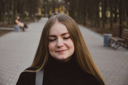 Portrait of a beautiful girl who walks along the alley in the park in a black jacket in the afternoonの写真素材