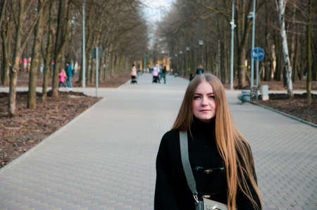 Portrait of a beautiful girl who walks along the alley in the park in a black jacket in the...