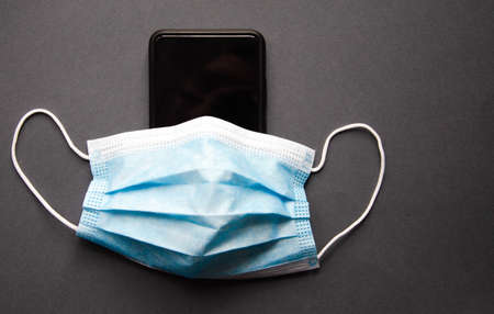Blue medical mask on a black smartphone. Protection, disinfection of the smartphone. The mask is...