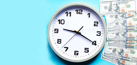 Analog white clock and dollars on a gray, yellow, blue background. Banknotes next to the clock, on top. Place for text. Business, are you ready? Copy Spaceの写真素材