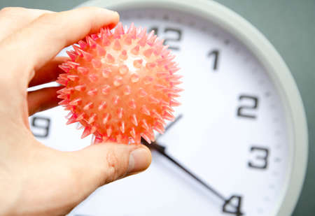 The male hand holds a red virus, the core of the coronavirus on the background of the clock. The...