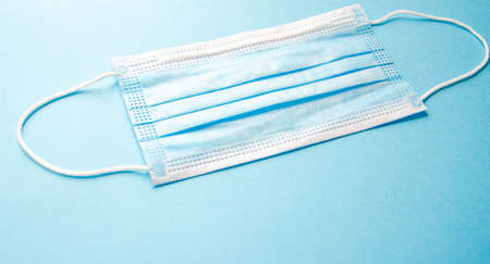 A blue medical mask lies alone on a blue background. Place for text.  Copy Space. COVID-19