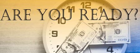 Analog clock and dollars on a wooden table. The inscription YOU ARE READY? Dollars in the form of a...