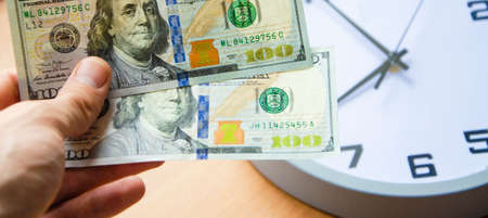 Analog clock and dollars on a wooden background. Banknotes in male hands 2 dollars on the background...