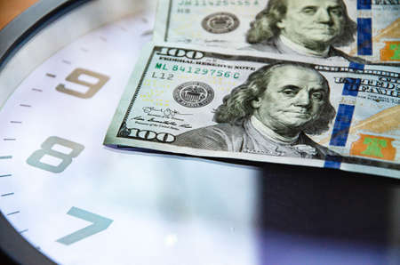 Analog clock and dollars on a wooden background. Banknotes are on the clock and next. Macro. Top and side view. The clock is 20:05, 08:05. Copy Spaceの写真素材