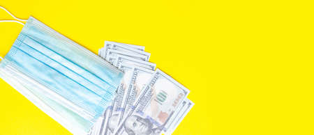 Blue medical mask with dollars on a blue, yellow, pink background. Mask and 100 dollar bills on a...
