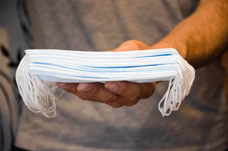 A man in a gray T-shirt is holding a large number of medical masks. Blue masks in a huge amount.  ...