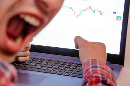 Trading on the exchange. Men's hands in a plaid shirt behind a laptop clenched into a fist....