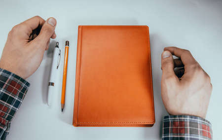 Men's hands, forearm hold a pen, notebook, smartphone. Hands write in notebook in a cell ideas,...
