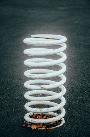 White big, giant spring on a black background. White very large and thick metal spring sticks out of the ground, attached to the ground, asphalt on a black background CopySpace Copy Spaceの写真素材