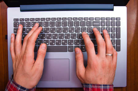 Men's hands in a shirt in a cage lie on the keyboard on a laptop from a first-person view from above. Hands are typing on a laptop. Freelancer, programmer. Typing in the blind. Work at the laptopの写真素材