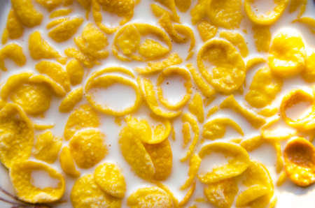 Cornflakes in the form of sliced chips with milk in a plate. Cereal in a spoon over a plate. Macro. Background texture. Breakfastの写真素材
