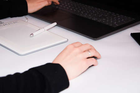 Female hands work on a graphic tablet. Hand holds stylus pen and draws. White graphic tablet. The...