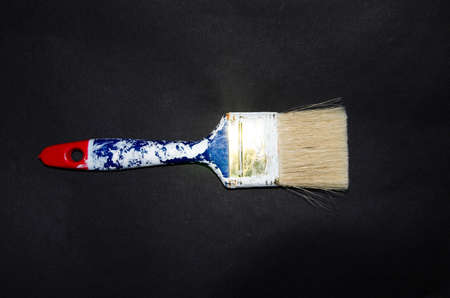 Used paint brush. Blue brush with a red tip in white paint. Macro photo. Repair brush in hand....