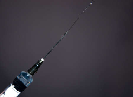 Syringe with a needle on a gray dark background. A drop, a stream flows from a syringe needle. Macroの写真素材