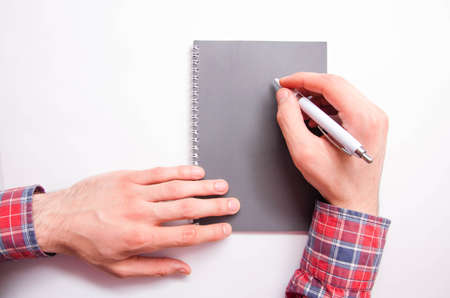 Men's hands in a checkered shirt hold a white pen and write on a notebook. Hands typing write ideas,...