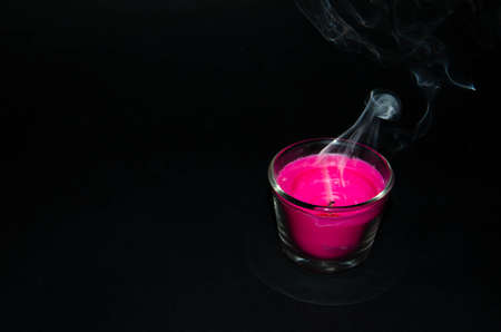 Bright pink candle in a glass jar on a black background. The candle is burning. Extinguished candle. Smoke from the candle. Hearth of fire. Tongue of flame. Macro.の写真素材