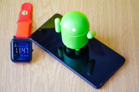 March 2020. Kramatorsk, Ukraine. Green android figurine on different backgrounds, together, near a smart watch, smartphone. Android on smart watch and  smartphoneのeditorial素材