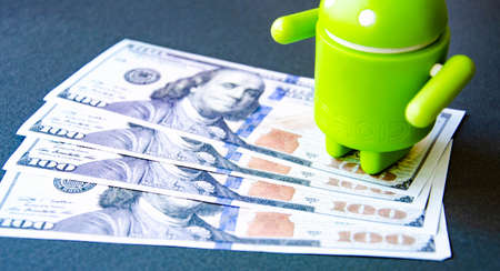 March 2020. Kramatorsk, Ukraine. Green android figurine on different backgrounds, along with dollars. Banknotes dollars in the background. Android and dollarsのeditorial素材