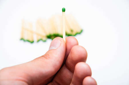 Wooden little matches with a green head. A manâs hand holds one match in his hand in the background a white background, and a bunch of matchesの写真素材