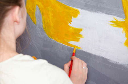Young girl designer draws a city drawing with paints on a gray wallの写真素材