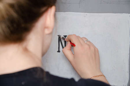 Young girl designer draws a city drawing with paints on a gray wallの写真素材