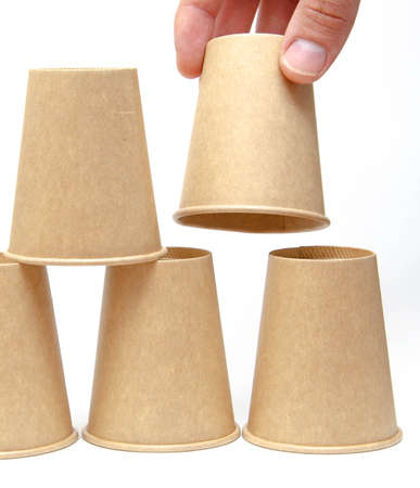 Brown paper cup for coffee, tea, a drink from environmental materials on a white background. The male hand builds a pyramid of cups in macro and overall plan. Place for text on the left and right.の写真素材