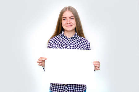 A young girl in a plaid shirt with long hair holds a large sheet, a frame for text in front of her, above herself, from the side. The girl demonstrates, offers, pointsの写真素材