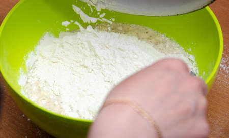 A female hand pours flour into a bowl with yeast and water and sugar. Making pizza dough