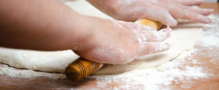 Female hands knead, knead the pizza dough. Dough, flour, cook, pizza. Girl rolls rolling pin dough