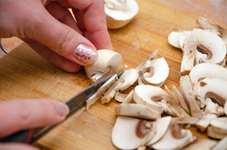 Mushrooms champignon sliced on board. Mushrooms in macro. Hand cuts mushrooms with a knifeの写真素材