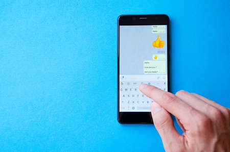 A male hand holds a smartphone, points a finger, types. Communication on a smartphone, correspondence. Place for text. Smartphone in hand on a blue background.の写真素材