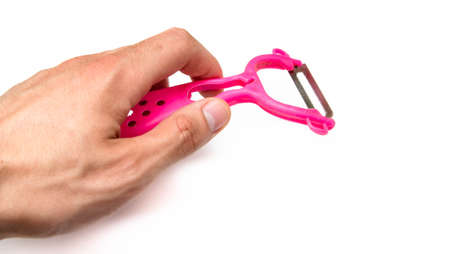 Pink peeler on a white background. Knife, peel for vegetables and fruits on a white drain and in a male handの写真素材