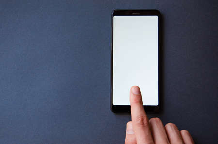 A male hand holds a smartphone, points a finger, types. Communication on a smartphone, correspondence. Place for text. Smartphone in hand on a gray background.の写真素材