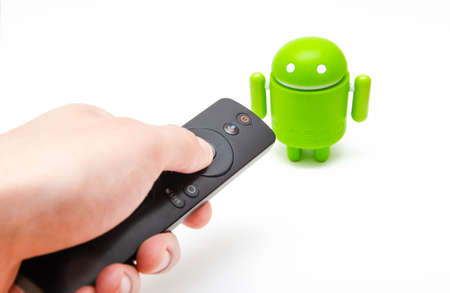 Android figure and tv remote. Green plastic figure on a white background, near the remote control from smart TV, set-top boxes. Male hand holds the remote and press pointing to androidのeditorial素材