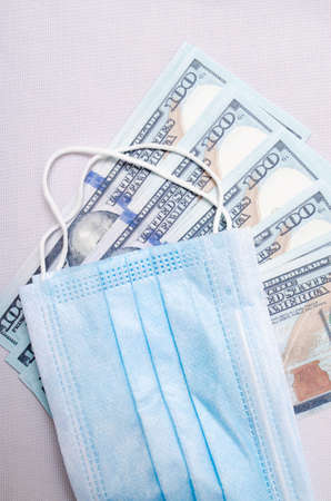 A medical blue mask lies on dollars with a face value of 100 dollars on a white background. Mask and dollarsの写真素材