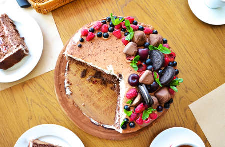 Chocolate cake in cocoa from above berries raspberries, black currant, biscuits, sweets on a round...