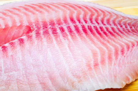One filet of hare fish, rabbit fish on a cutting board in macro. Dorado fillet, telapia. Raw fish, seafood in macro. Top and side view. Large approximation of filetの写真素材