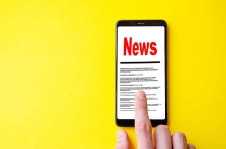 News. Reading the news. The inscription red news on the smartphone screen lies on a yellow...