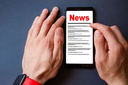 News. Reading the news. The inscription red news on the smartphone screen lies on a black background. Male hand holds a smartphone, clicks, leafs through the newsの写真素材