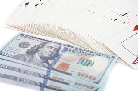 Dollars and playing cards. Banknotes with a face value of 100 dollars are lying on a white background in a pile, a bunch of flowers, on top is a deck of cards, an ace of hearts from above and at an angleの写真素材