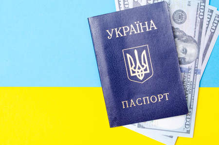 Ukrainian passport on a blue-yellow background. Dollars of 100 dollars are inside the passport at different angles. Packport with dollars on the Ukrainian flagの写真素材