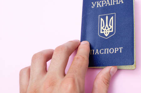 Ukrainian passport on a pink background. Man's hand holds a Ukrainian passport in hand, gives the passport. The passport of the citizen of Ukraine in the macro. Passport general plan and close-upの写真素材