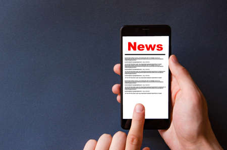 News. Reading the news. The inscription red news on the smartphone screen lies on a black background. Male hand holds a smartphone, clicks, leafs through the newsの写真素材